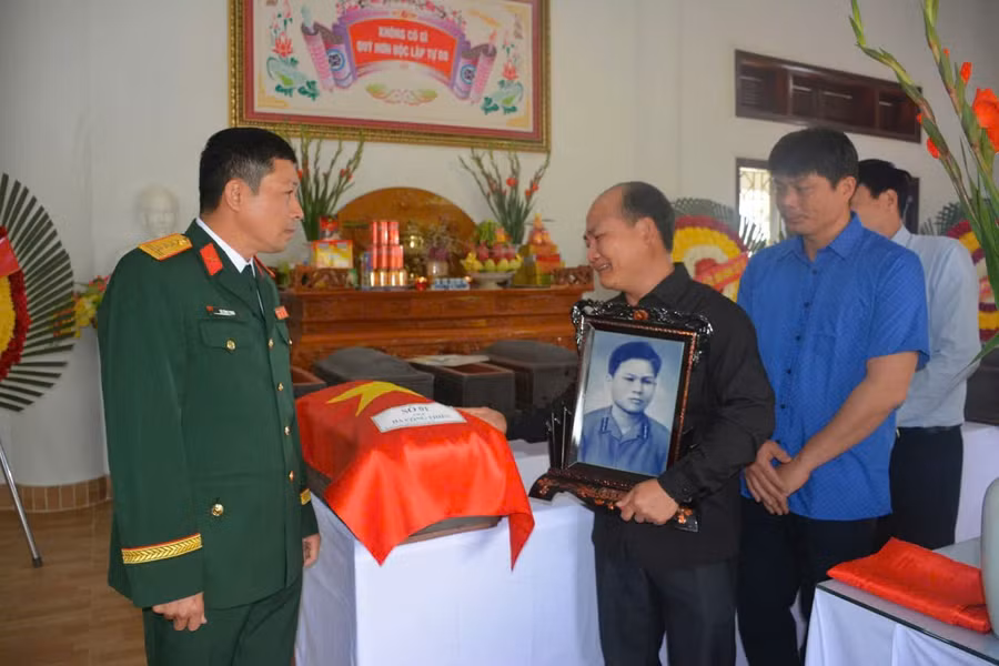 Đại tá Dư Công Thịnh (bên trái) bàn giao hài cốt liệt sĩ Hà Công Thiên cho gia đình; ông Hà Công Lực ôm di ảnh người thân.
