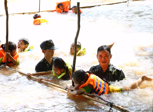 Trung tá Đặng Văn Trí - Đội phó đội vận động quần chúng Đồn biên phòng Bình Thạnh (người không đội nón) trực tiếp xuống sông cùng các chiến sĩ khác dạy bơi cho các em nhỏ xã Tân Hội và xã Bình Thạnh (ảnh: Phú Quí)