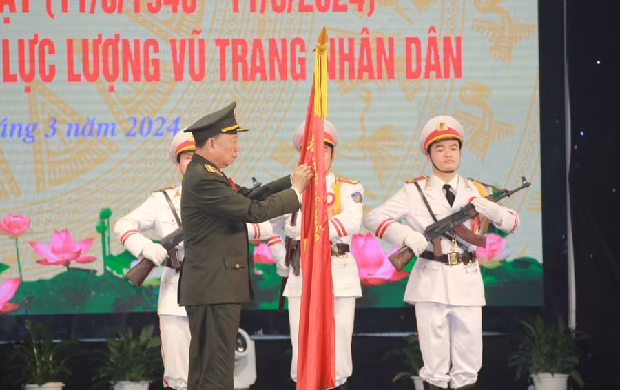 Đại tướng Tô Lâm gắn huy hiệu Anh hùng Lực lượng vũ trang nhân dân lên lá cờ truyền thống của Công an tỉnh Nghệ An. (Ảnh: CANA)