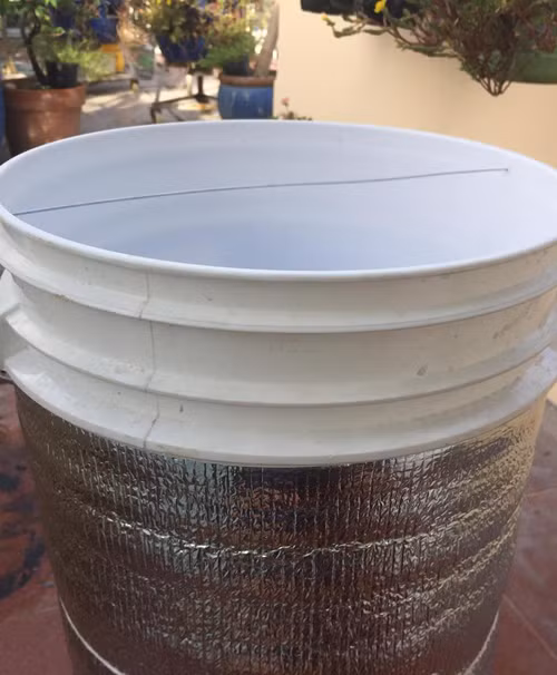 Cách trồng dưa lưới “bán thủy canh” trên sân thượng ảnh 6 Trên miệng thùng, anh khoan một lỗ nhỏ và dùng dây kẽm kéo qua. Đây là đoạn dây sẽ làm điểm tựa cho gốc không bị gió lung lay.Mặt ngoài của thùng sơn được bọc cách nhiệt giúp cho nước trong thùng Earthbox không tăng cao.