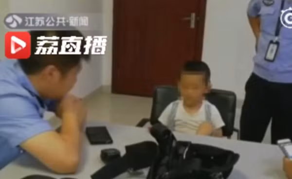 Kaikai ở đồn cảnh sát chờ bố tới đón. Kaikai ở đồn cảnh sát chờ bố tới đón. Ảnh: Jiangsu TV.