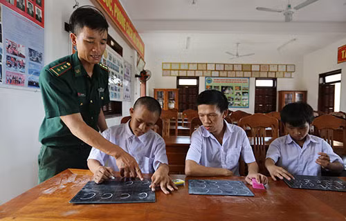 Thượng úy Lê Văn Chính bày cho hoc sinh viết chữ. Ảnh: Đắc Thành.