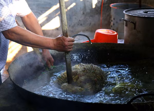 Họ dùng chày dìm lưới đựng vịt ngập trong nước sôi.