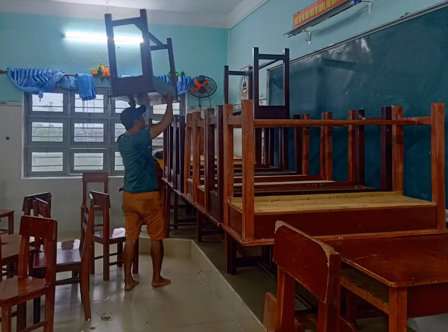 Thầy giáo đang kê cao bàn ghế để tránh nước lụt. Thầy giáo đang kê cao bàn ghế để tránh nước lụt.