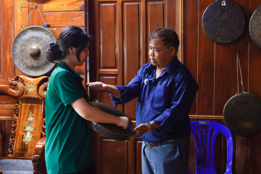 Ông Điểu Sa Réc hướng dẫn Lan Anh (sinh viên năm 2, Trường Đại học Khoa học Xã hội và Nhân văn) đánh cồng chiêng. Ảnh: H.L - A.N.