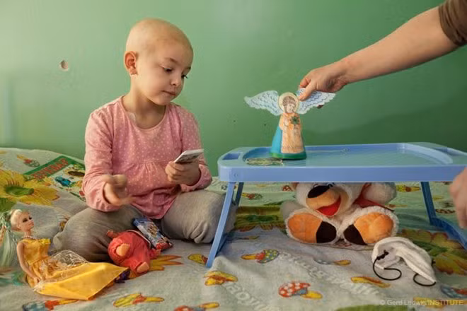 Veronika, 5 tuổi, mắc bệnh máu trắng và phải điều trị tại một bệnh viện ở Kiev. Khi thảm họa Chernobyl xảy ra vào năm 1986, cô Yelena, mẹ của em, mới 4 tuổi và sống gần nhà máy. Theo các bác sĩ, nhiều phụ huynh là nạn nhân trực tiếp của vụ nổ. Do nhiễm phóng xạ nên họ sinh ra những đứa con mắc bệnh hoặc phát triển không bình thường. Ảnh: Long Shadow Of Chernobyl 1