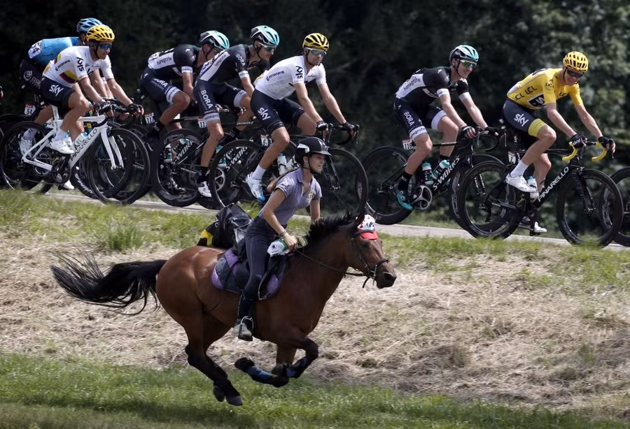 Một phụ nữ trẻ cưỡi ngựa bên cạnh đội đua xe đạp tham gia Tour de France lần thứ 104