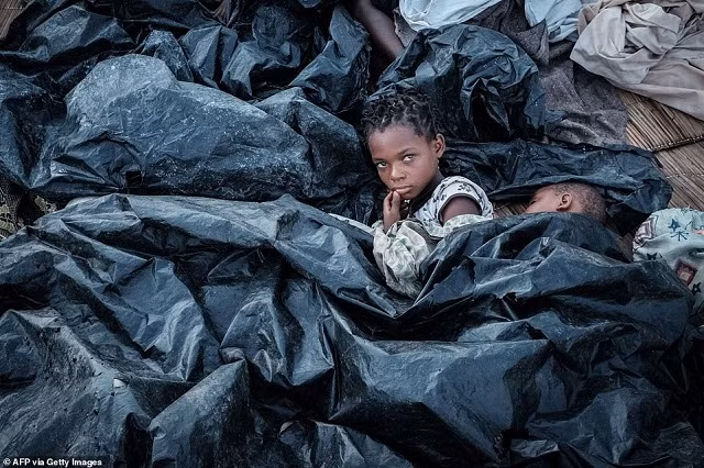 Enia Joaquin Luis, 11 tuổi, thức dậy bên cạnh em gái Luisa, 6 tuổi, dưới tấm nhựa để bảo vệ bản thân khỏi mưa khi họ ở trong nơi trú bão tại khán đài của Ring ground ở Buzi, Mozambique, vào ngày 23 tháng 3 Enia Joaquin Luis, 11 tuổi, thức dậy bên cạnh em gái Luisa, 6 tuổi, dưới tấm nhựa để bảo vệ bản thân khỏi mưa khi họ ở trong nơi trú bão tại khán đài của Ring ground ở Buzi, Mozambique, vào ngày 23 tháng 3