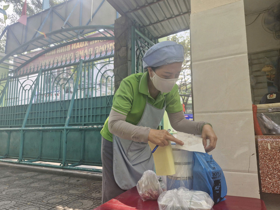 Bảo mẫu Trường Tiểu học Tân Quy (phường Tân Hưng) nhận đồ ăn phụ huynh mang đến cho con trưa 29/1.