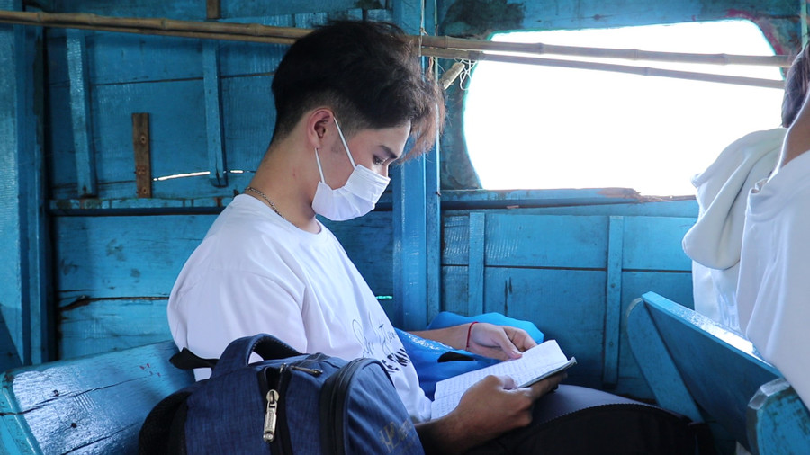 Học sinh ấp đảo tranh thủ ôn bài khi ngồi trên đò, di chuyển sang trung tâm xã Thạnh An. Ảnh: Bùi Vân