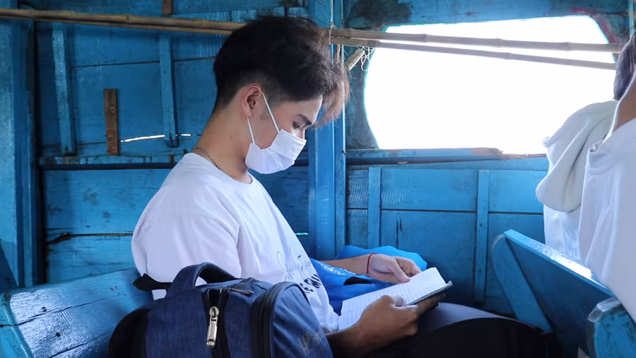 Học sinh ấp đảo tranh thủ ôn bài khi ngồi trên đò, di chuyển sang trung tâm xã Thạnh An. Ảnh: Bùi Vân