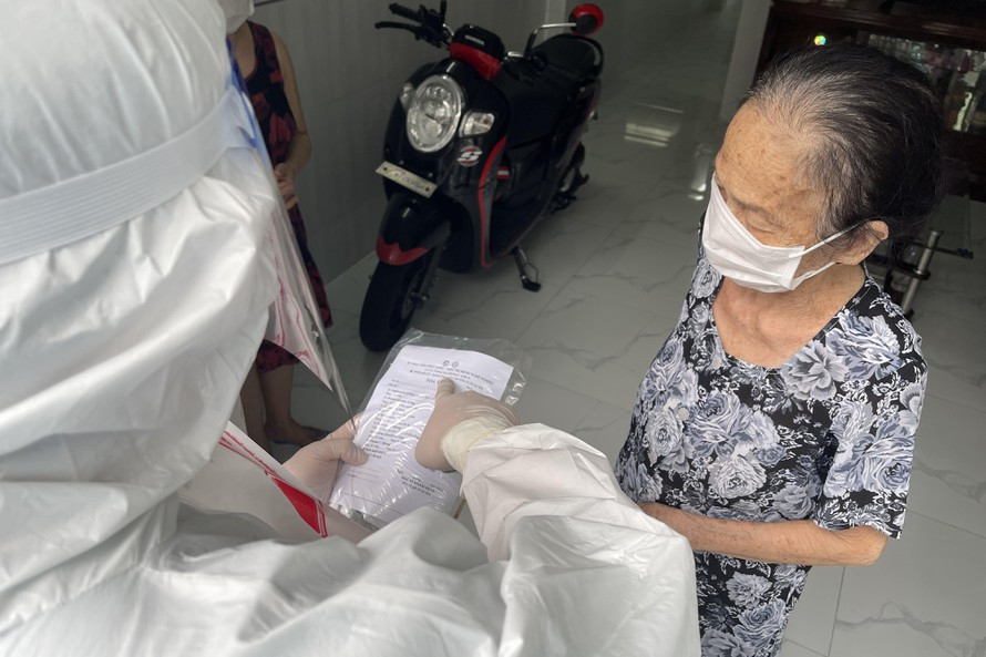 Nhân viên y tế phát túi thuốc điều trị tại nhà và hướng dẫn cho F0 sử dụng. Ảnh: Vân Sơn.