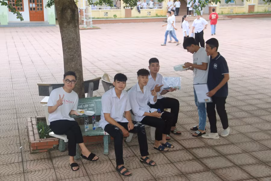 Học sinh tại điểm thi THPT Chiềng Sinh ngồi ghế đá giữa sân trường với tâm thế thoải mái.