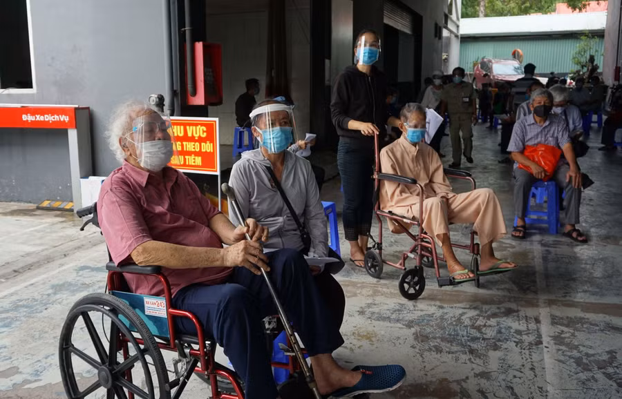 Các cụ ông, cụ bà được các bác sĩ khám sức khỏe rất kỹ trước khi vào tiêm. Người đến tiêm không phải chờ đợi lâu và được hướng dẫn ngồi giãn cách. Trong ảnh: Tại điểm tiêm của Bệnh viện Quân Y 175, nhiều cụ ông cụ bà sức khỏe yếu, đi lại khó khăn nhưng vẫn rất vui mừng đi tiêm vắc xin. Nguồn: Báo Tin tức.