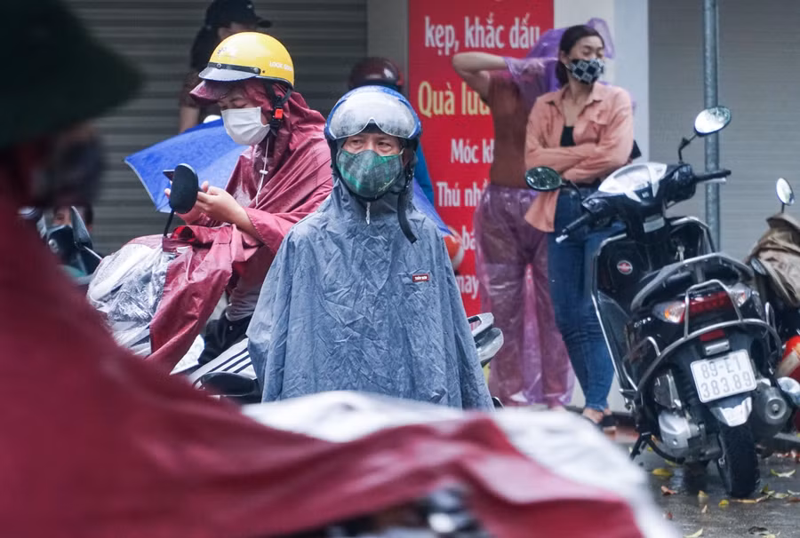 Một phụ huynh tỏ vẻ lo lắng trong lúc chờ đợi con dưới mưa.