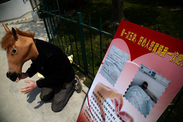 Bố làm "ngựa người" kiếm tiền chữa bệnh cho con ảnh 1 Chen Yuntao, wearing a horse head mask, kneels beside a billboard advertising 5 yuan ($0.8) rides on his back on a road in Hefei, capital city of East China