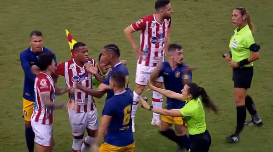 Jean Carlos bị đồng đội và cầu thủ đối phương khống chế.