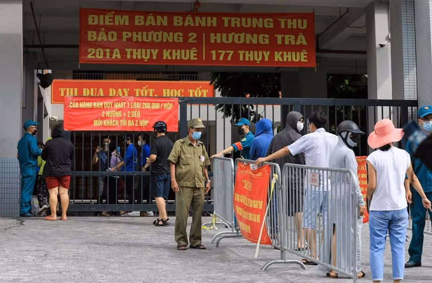 Lực lượng dân phòng hướng dẫn người dân xếp hàng đảm bảo giãn khoảng cách cần thiết, mỗi lượt vào mua bánh chỉ cho 10 người vào. Ảnh: TTXVN.