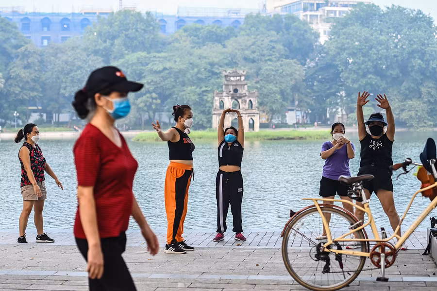 Người dân tập thể dục trên vỉa hè Hồ Gươm. Phía đối diện, tại khu vực vườn hoa Lý Thái Tổ, cơ quan chức năng vẫn căng dây hạn chế ra vào. Nguồn: VNE.