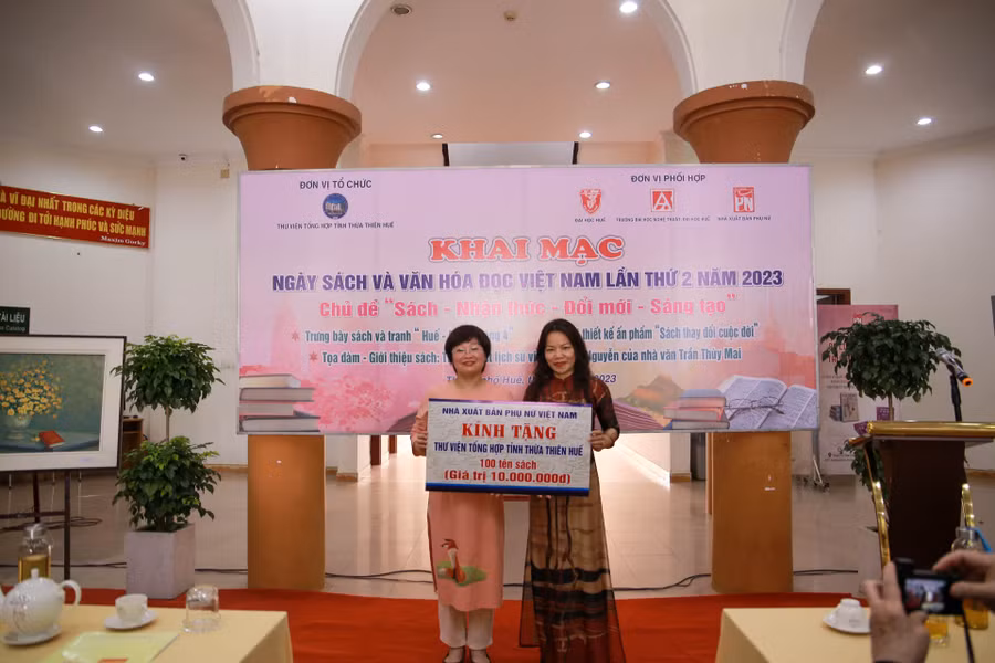 Bà Khúc Thị Hoa Phượng, Giám đốc - Tổng biên tập Nhà xuất bản Phụ nữ Việt Nam (bên trái) trao tặng 100 tên sách cho bà Hoàng Thị Kim Oanh – Giám đốc Thư viện Tổng hợp tỉnh Thừa Thiên - Huế (bên phải) tại lễ khai mạc.