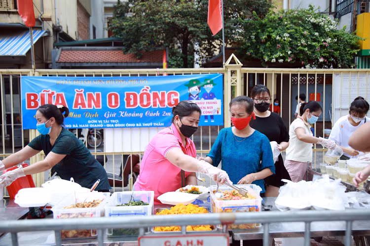 Ý tưởng "bữa cơm 0 đồng" của bà Giang (làng Phú Đô, Nam Từ Liêm, Hà Nội) được triển khai với sự hỗ trợ của các đoàn viên thanh niên phường Phú Đô tặng những suất cơm “0 đồng” để hỗ trợ người dân nghèo trong những ngày giãn cách. Trong ảnh: Bà Trần Thị Giang (áo hồng) đang chuẩn bị những phần cơm "0 đồng". Nguồn: Báo Tin Tức.
