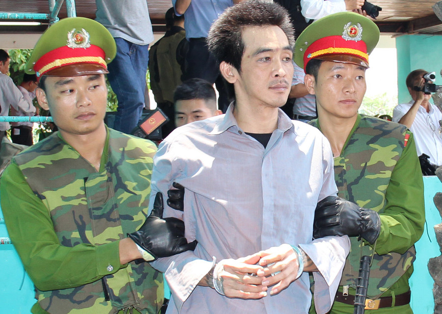 Hai cảnh sát mang bao tay, áo dài tay và khoác thêm áo giáp khi áp giải Tuấn Em. Ảnh: Việt Tường.