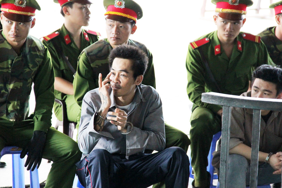 Gã giang hồ nhìn về phía những người ngồi sau lưng bàn thư ký và dùng tay ra ký hiệu. Ảnh: Việt Tường.