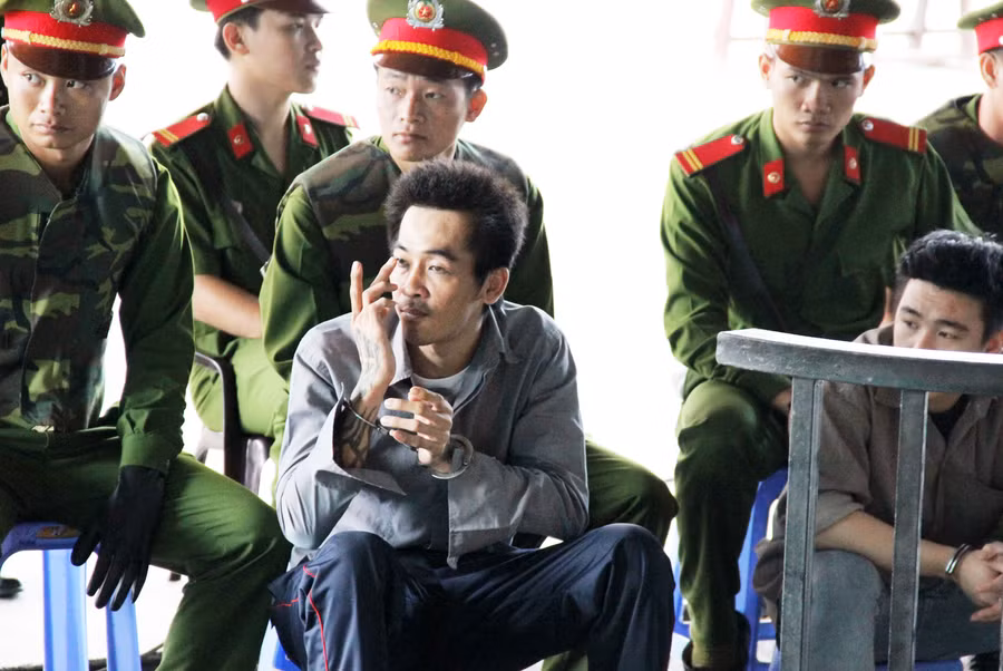 Gã giang hồ nhìn về phía những người ngồi sau lưng bàn thư ký và dùng tay ra ký hiệu. Ảnh: Việt Tường.