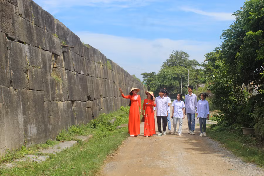 Hướng dẫn viên (bìa trái) giới thiệu về bức tường bằng đá bao quanh Thành Nhà Hồ.