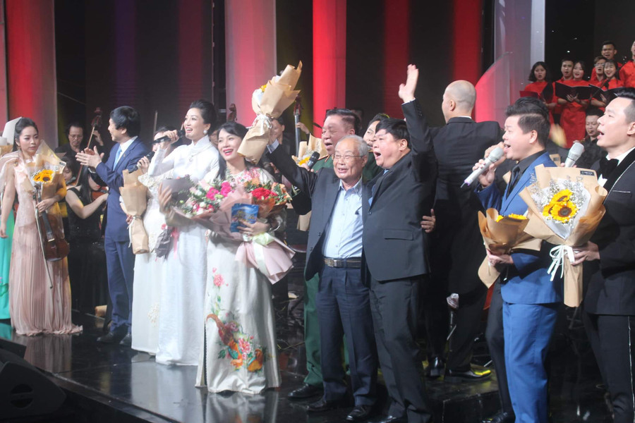 Nhạc sĩ Phạm Minh Tuấn (người cầm hoa giơ lên) cùng các vị khách mời và ca sĩ thể hiện ca khúc &apos;Bài ca không quên&apos; trong đêm nhạc &apos;Bài ca không quên&apos; do Trung tâm Phát thanh - Truyền hình Quân đội tổ chức năm 2022. Ảnh: Trần Công Thủy.