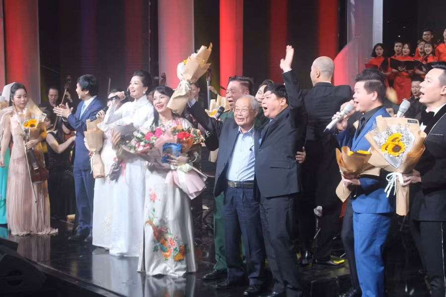 Nhạc sĩ Phạm Minh Tuấn (người cầm hoa giơ lên) cùng các vị khách mời và ca sĩ thể hiện ca khúc 'Bài ca không quên' trong đêm nhạc 'Bài ca không quên' do Trung tâm Phát thanh - Truyền hình Quân đội tổ chức năm 2022. Ảnh: Trần Công Thủy.