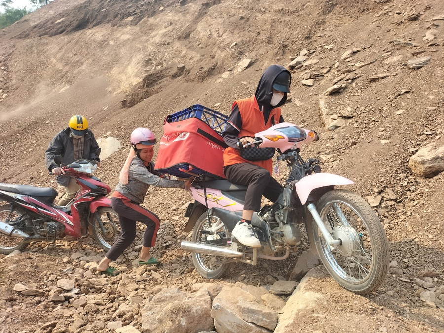 Người dân đẩy xe giúp đỡ nhau vượt qua đoạn đất đá chắn ngang giữa đường tránh.