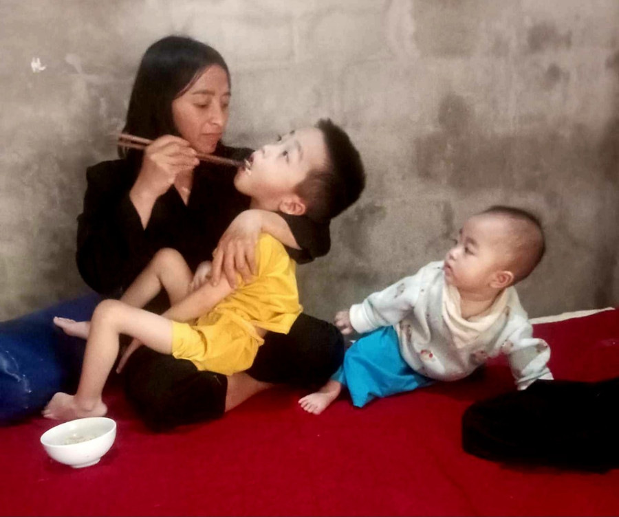 Người mẹ thiểu năng bón từng thìa cháo cho đứa con bị bại não.