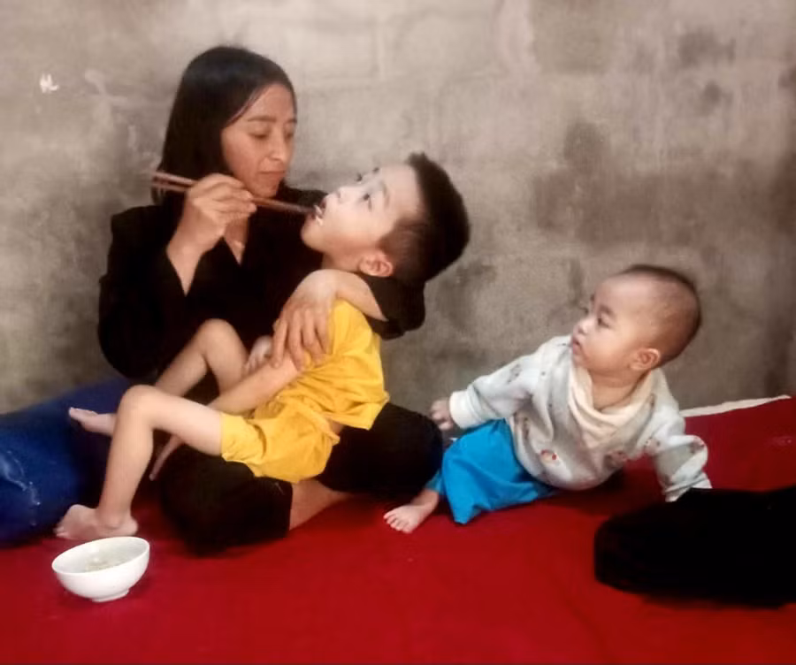 Người mẹ thiểu năng bón từng thìa cháo cho đứa con bị bại não.