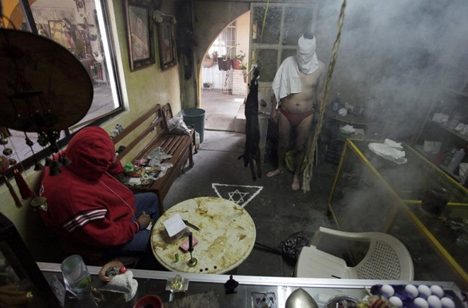 Pháp sư (trái) Joaquin cầu nguyện trong khi người đàn ông đồng tính đứng bên con dê dùng để hiến tế trong một căn nhà tại thành phố Saltillo, Mexico. Pháp sư (trái) Joaquin cầu nguyện trong khi người đàn ông đồng tính đứng bên con dê dùng để hiến tế trong một căn nhà tại thành phố Saltillo.