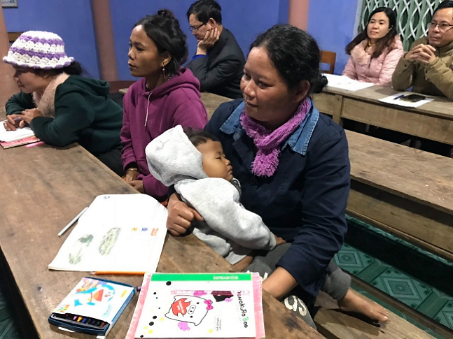 Một học viên nữ vừa tranh thủ vừa chăm con, vừa tham gia lớp học xóa mù chữ.