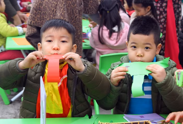 Hai trẻ này đang cùng nhau thi thổi voi giấy sau khi hoàn thành làm chú voi bằng giấy.