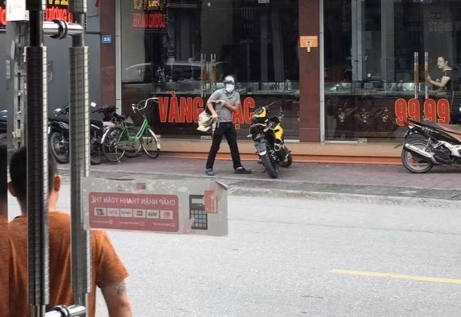 Tên cướp cầm súng khi bước ra từ tiệm vàng. Ảnh: Khánh Nhung.