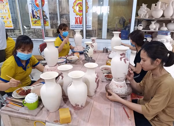 Các nghệ nhân vẽ hoa văn trên sản phẩm gốm. Ảnh: NSNA Trần Hồng.