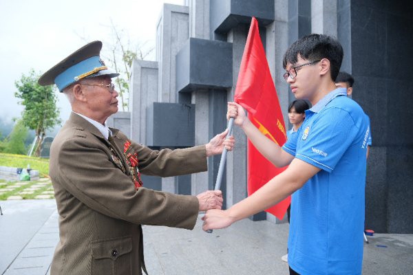 Cựu chiến sĩ Điện Biên Phạm Đức Cư trao cờ chiến thắng cho học sinh tham gia trải nghiệm &quot;Chúng em làm chiến sĩ&quot;.