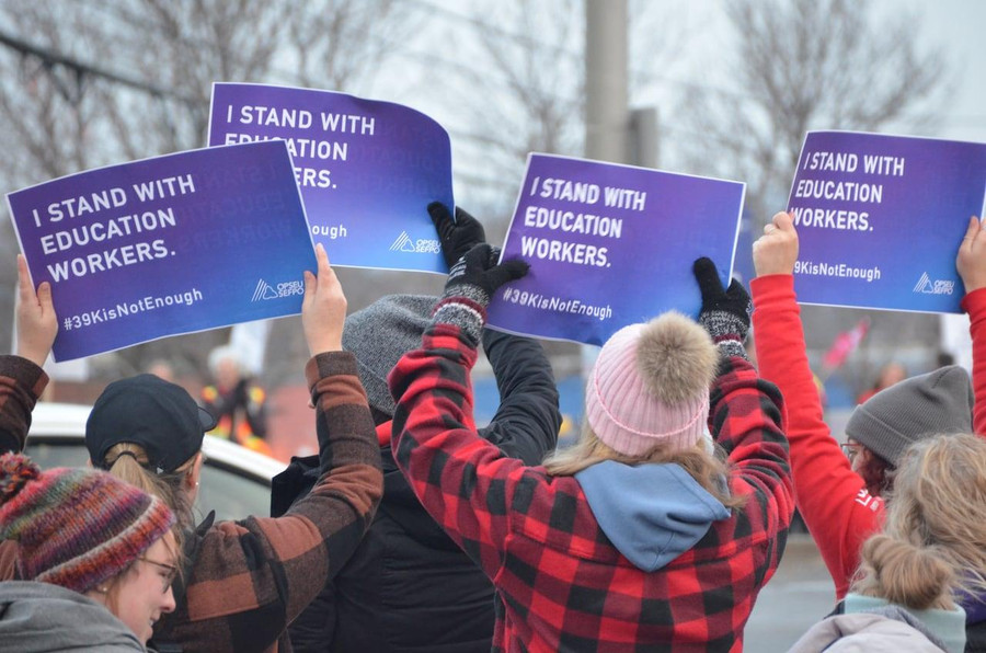 Đám đông cầm biểu ngữ 'I stand with education workers' (dịch: Tôi đứng về phía nhân viên giáo dục).