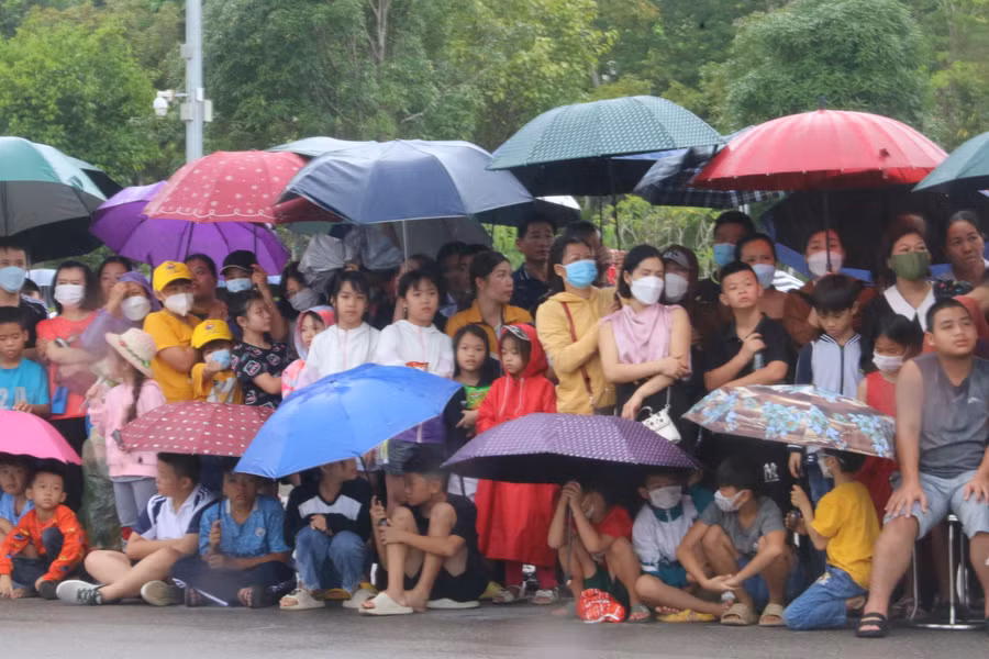 Đông đảo người dân và trẻ nhỏ che ô đứng dưới mưa cổ vũ tại Quảng trường Tây Bắc.