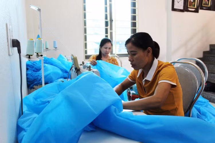 Chị Lương Thị Toan (ngoài cùng bìa phải) tranh thủ may đồ bảo hộ phòng dịch Covid-19, với tiền công chỉ 4.000 đồng/bộ.