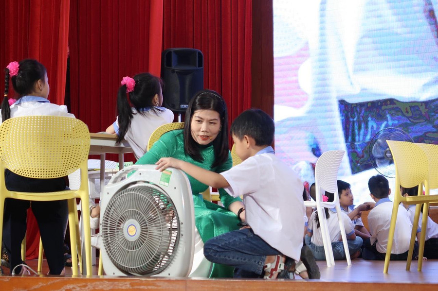 Cô Mai kiểm tra phần thực hành sử dụng quạt đúng cách của học sinh.