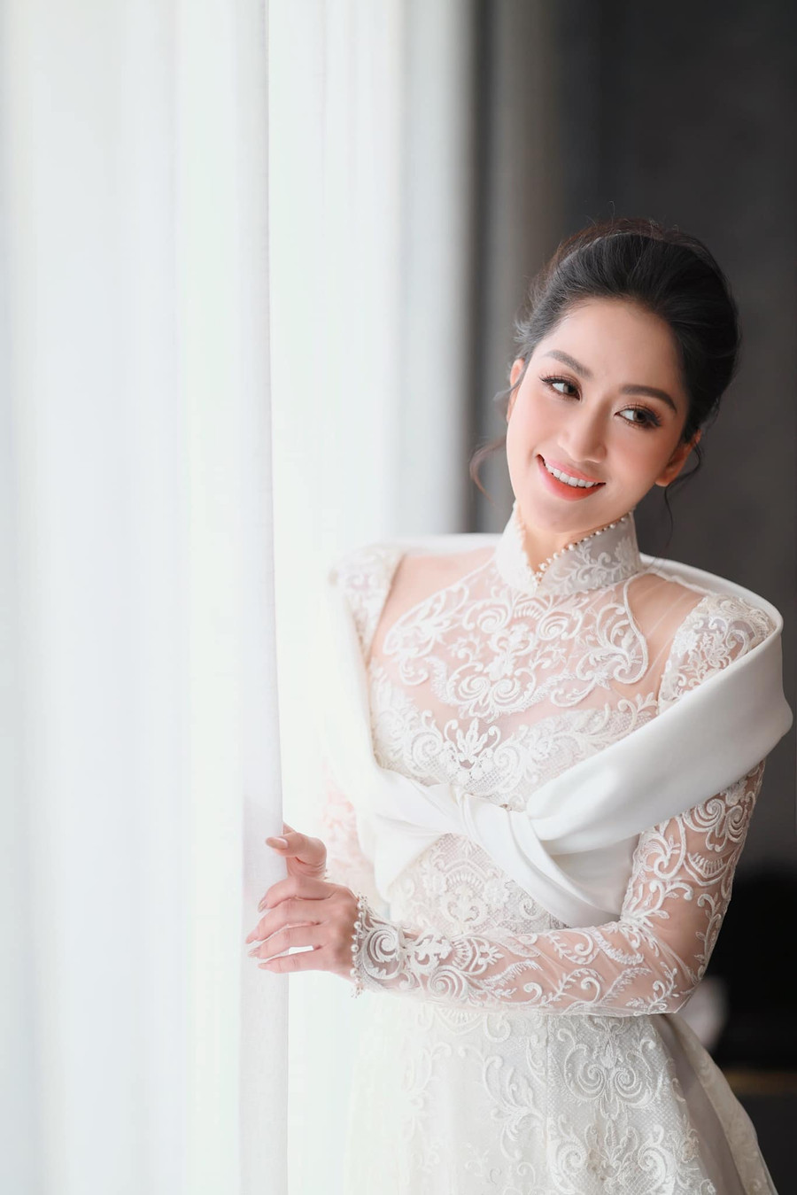 Tại lễ ăn hỏi và rước dâu được thực hiện tại nhà riêng, Khánh Thi diện áo dài xuyên thấu, được trang trí bằng lớp vải ren cầu kỳ, cổ áo đính ngọc trai giúp tôn lên vẻ đẹp nữ tính.