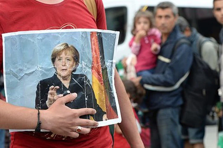 Ảnh Thủ tướng Đức Angela Merkel trên tay một người di cư tới Đức. Ảnh: Getty/Express.