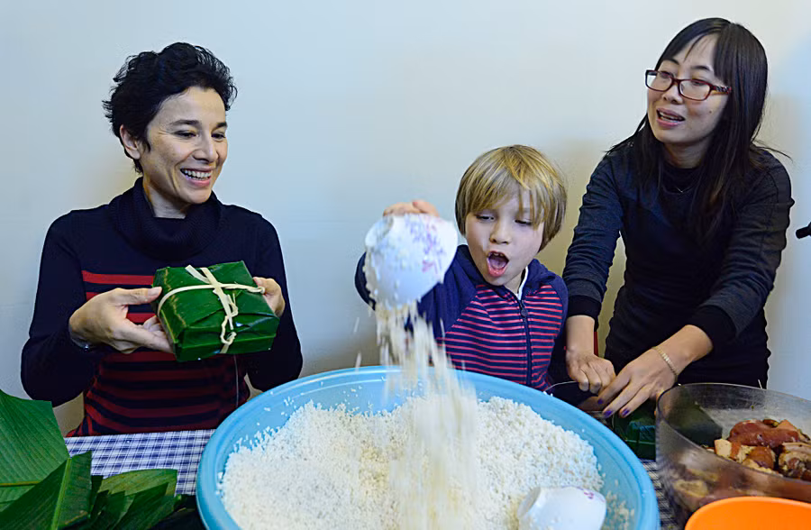 Phu nhân đại sứ, bà Eva Nguyễn Bình (trái) và con trai cũng tự tay gói bánh. Cậu bé tỏ ra rất thích thú khi lần đầu tham gia gói những chiếc bánh chưng xinh xắn.