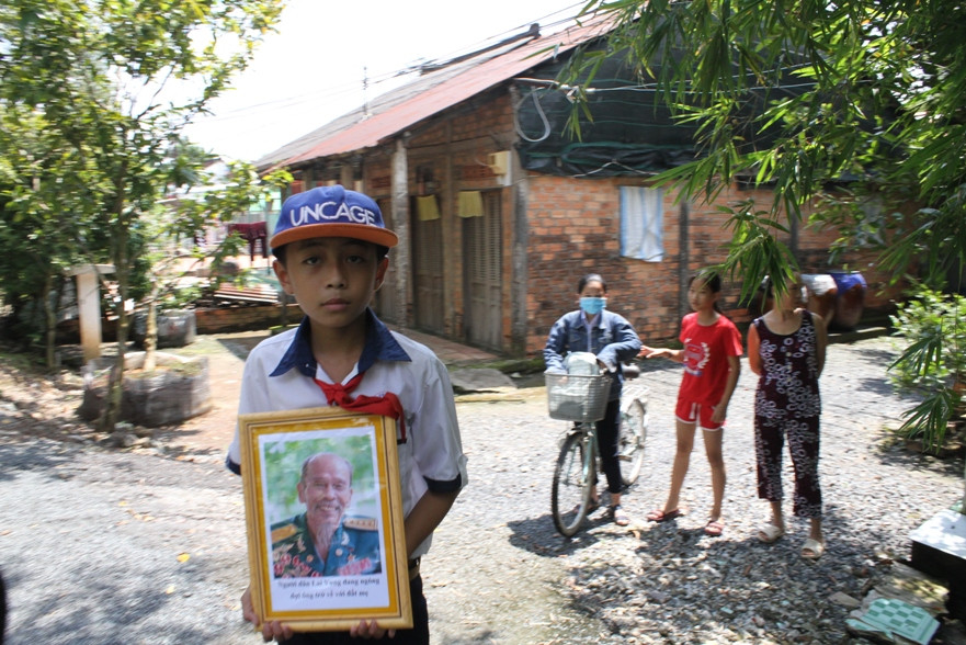 Một học sinh cầm trên tay di ảnh đứng bên đường đưa tiễn ông Bảy.