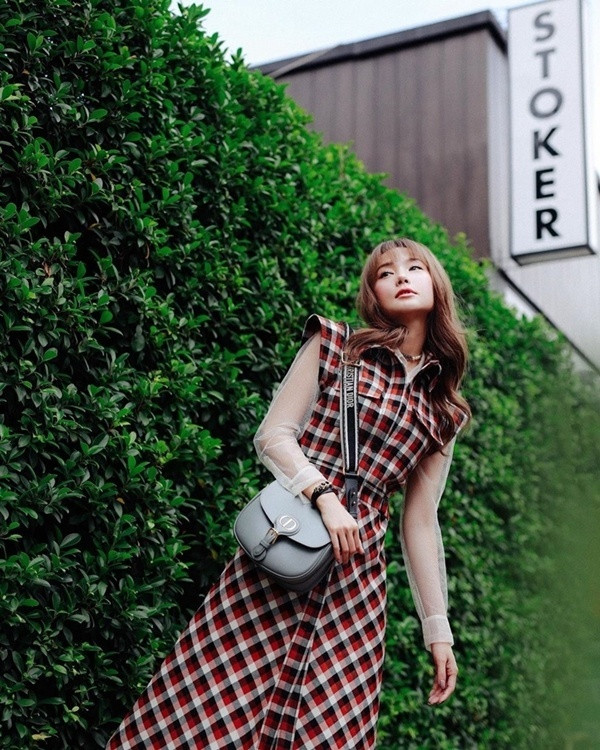 Minh Hằng trẻ trung khi phối layer chiếc đầm kẻ caro với áo xuyên thấu. Người đẹp tạo điểm nhấn cho bộ cánh street style bằng chiếc túi Dior Bobby, phiên bản màu xám.
