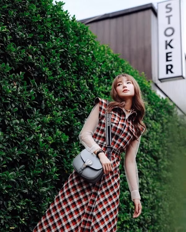 Minh Hằng trẻ trung khi phối layer chiếc đầm kẻ caro với áo xuyên thấu. Người đẹp tạo điểm nhấn cho bộ cánh street style bằng chiếc túi Dior Bobby, phiên bản màu xám.